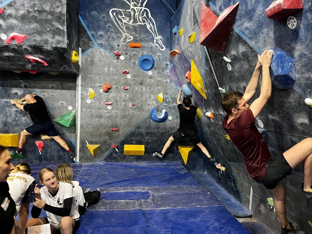 Группа участников тренируется на скалодроме, несколько человек в разных упражнениях